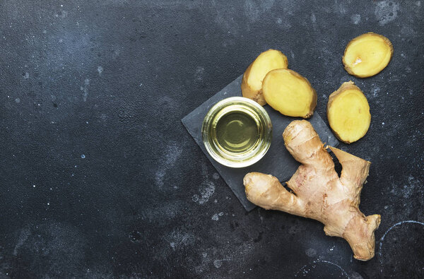 Ginger oil and fresh ginger root, gray kitchen table, copy space, top view