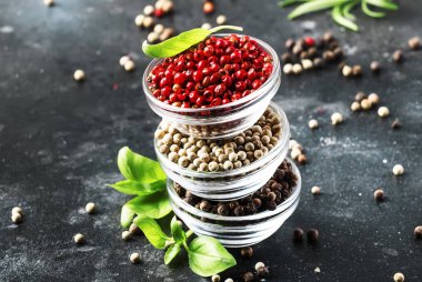 Biber seti. Kaselerde siyah, beyaz ve pembe gül biber, gri mutfak masasında çeşitli baharatlar, seçici odak