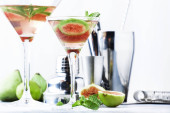 Růžový fígl Martini v střílené sklenici na šedém stole s čárovým nástrojem, selektivní zaostření