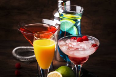 Renkli yaz kokteylleri. Soğuk alkollü içecekler ve içecekler: mimoza, kozmopolit, ahududu margarita ve bar araçları ile ahşap masa arka plan üzerinde mavi hawaii