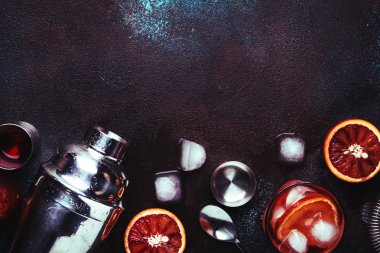 Kuru cin, kırmızı vermut ve kırmızı acı, kanlı portakal dilimi ve buz küpleri ile Negroni alkollü kokteyl içecek. Kahverengi bar sayacı arka plan, çelik çubuk araçları, üst görünüm, kopyalama alanı ile