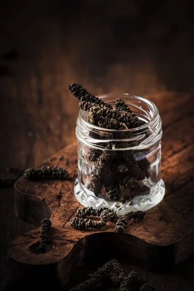 Fragrant long pepper spilling out of glass jar, vintage kitchen table background, selective focus