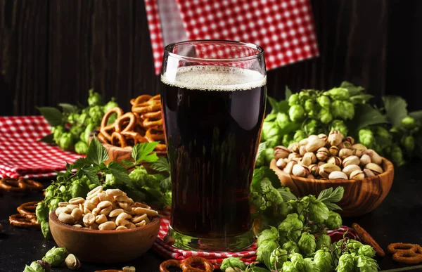 ガラス 新鮮な緑のホップと塩味のスナックとナッツ 秋のビール祭のコンセプト 暗い背景 選択と集中の鉢に暗いドイツ ビールを注いだ — ストック写真