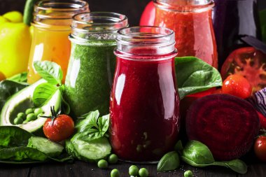Çok renkli vegan sebze suları ve smoothies gelen domates, havuç, biber, lahana, ıspanak, pancar rustik mutfak masası, vejetaryen yiyecek ve içecek kavramı, seçici odak cam şişelerde