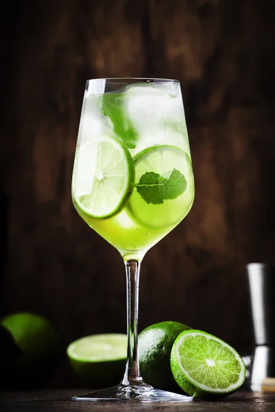 Martini royale alcoholic cocktail with white vermouth, prosecco, lime, mint and ice. Old wooden table background, bar tools, selective focus. All names refer to cocktails, not trademarks