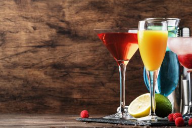 Renkli yaz kokteylleri. Soğuk alkollü içecekler ve içecekler: mimoza, kozmopolit, ahududu margarita ve bar araçları ile ahşap masa arka plan üzerinde mavi hawaii