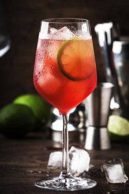 Kırmızı acı tonik, limon ve buzlu Campari tonik kokteyli. Eski ahşap masa arkaplanı, bar araçları, seçici odaklanma. Tüm isimler kokteyllere yöneliktir, markalara değil.
