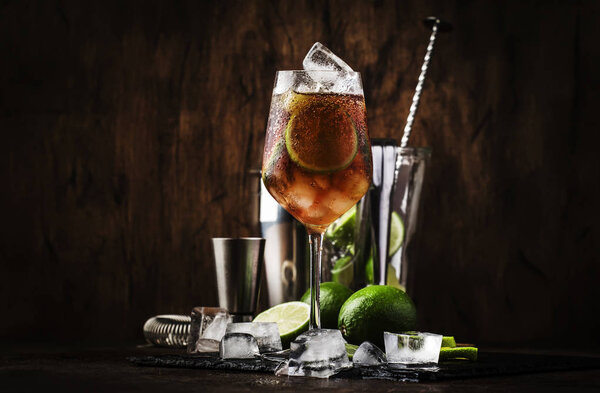 Alcoholic cocktail Long Island with vodka, gin, tequila silver, white rum, liqueur, sugar syrup, lemon juice, cola and ice cubes, vintage bar wooden counter background, selective focus
