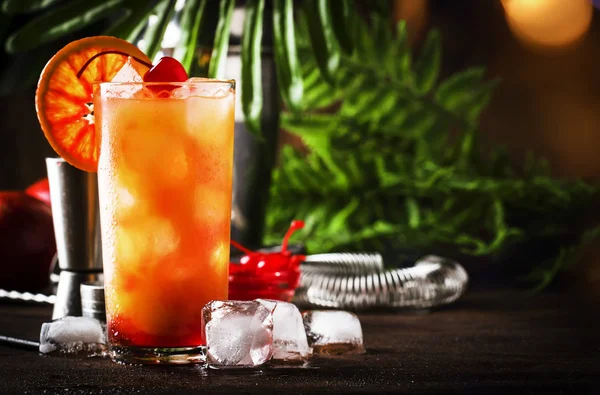 Tequila sunrise alcoholic cocktail with silver tequila, grenadine syrup, orange and ice cubes. Wooden bar counter background. Summer mood concept. Selective focus. Copy space