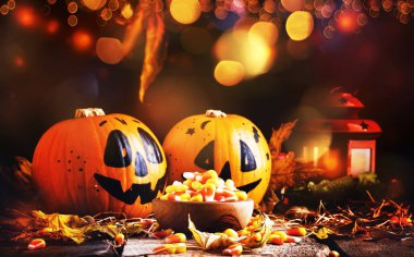 Cadılar Bayramı şenlikli kompozisyon tatlı Mısır kase ve gülümseyen kabaklar korumaları, fener, saman ve düşmüş yaprakları koyu ahşap arka plan, rustik tarzı, seçici odak ile