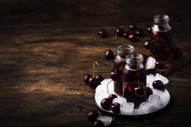 Kiraz suyu, vintage ahşap masa üzerinde cam şişelerde buz ile soğuk içecek, düşük anahtar, kopya alanı