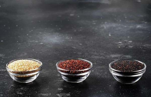 Black, white and red quinoa in bowls, raw quinoa groats set on gray kitchen table, copy space, selective focus