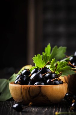 Ahşap kaselerde taze siyah kuş üzümü, siyah mutfak masası arka planda, kopyalama alanı, seçici odak
