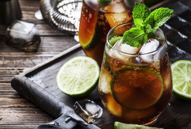 Altın rom ile Küba libre alkol kokteyl, limon suyu, kola, kireç ve buz, koyu bar sayacı arka plan, bar araçları, metin için yer