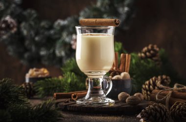 Yeni Yıl veya Noel Eggnog kokteyl - sıcak kış veya süt, yumurta ve koyu rom ile sonbahar içki, tarçın ve hindistan cevizi ile ahşap arka plan, şenlikli dekorasyon bir bardak serpilir