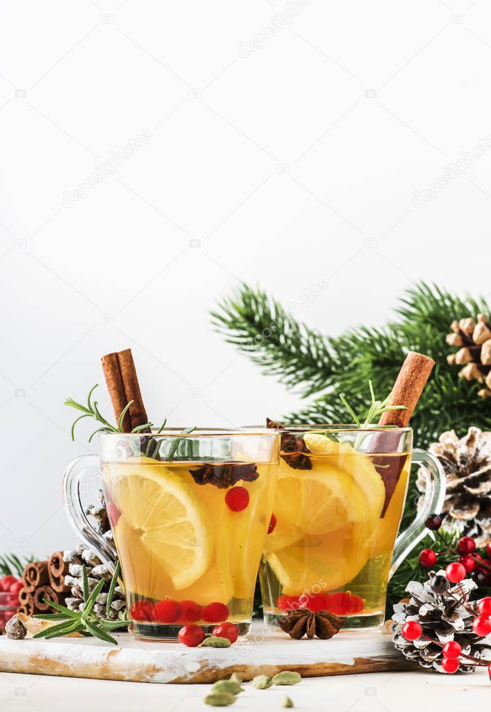Winter hot tea with lemon, cranberries, herbs and spices for Christmas or New Year evening, white background, copy space, selective focus