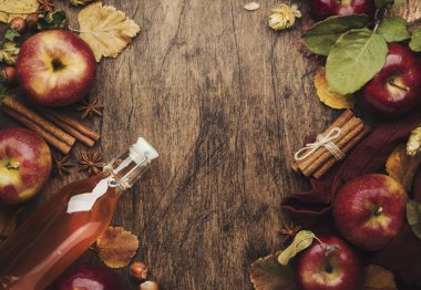 Elma sirkesi. Ahşap masa arkasında bir şişe taze elmalı organik sirke, tarçın çubukları, anason yıldızı, fındık ve düşen yapraklar. Sağlıklı organik yiyecekler. Boşluğu kopyala