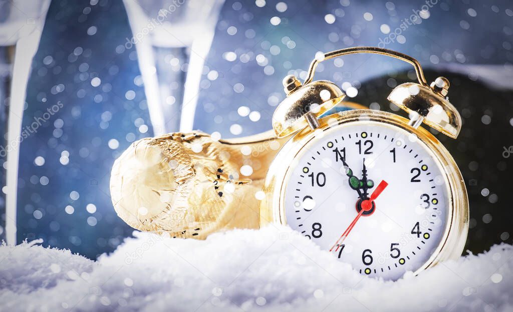 Christmas or New Year background with golden clock in snowdrifts, champagne bottle and glasses on blue background with festive lights. Counting the last moments before the countdown to midnight.