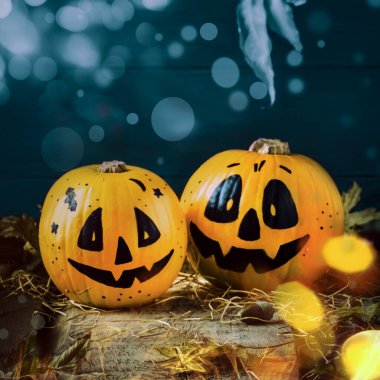 Gülen balkabaklarıyla Cadılar Bayramı kompozisyonu. Işıklı, fenerli, samanlı ve düşmüş yapraklı koruyucular. Koyu ahşap arka planda, kırsal tarzda, seçici odaklı.