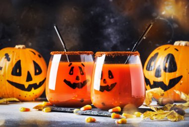 Cadılar Bayramı turuncu şenlik içeceği ve balkabağı koruyucuları Gri sonbahar arka planında Tatlı mısır, düşmüş yapraklar ve ateş ışıkları, seçici odaklı 