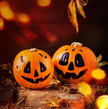 Gülen balkabaklarıyla Cadılar Bayramı kompozisyonu. Işıklı, fenerli, samanlı ve düşmüş yapraklı koruyucular. Koyu ahşap arka planda, kırsal tarzda, seçici odaklı.