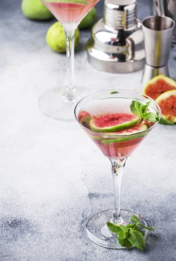Pembe incirli alkollü martini bardakta gri masada bar aletleriyle, kopyalama alanı