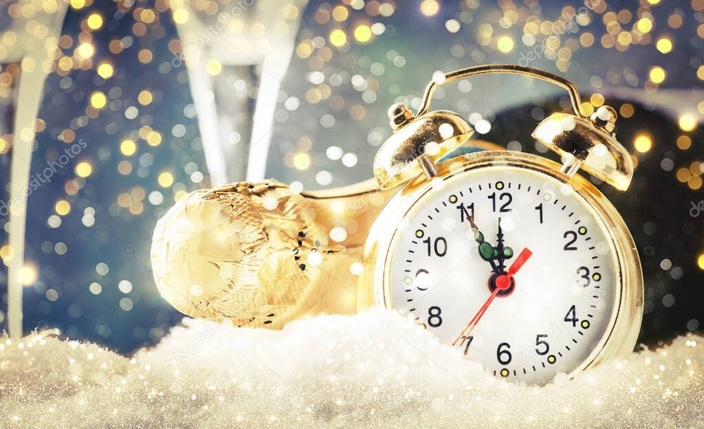 Christmas or New Year background with golden clock in snowdrifts, champagne bottle and glasses on blue background with festive lights. Counting the last moments before the countdown to midnight.