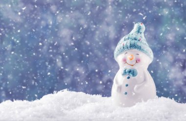 Kar yığınındaki porselen kardan adam heykelciği, Noel ya da yeni yıl arkaplanı kar taneleri ve ışıklarıyla