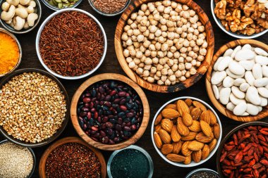 Süper yiyecekler, baklagiller, fındıklar, tohumlar ve tahıllar tahta arka planda kaselerde. Chia, spirulina, fasulye, goji üzümü, kinoa, zerdeçal, mung fasülyesi, karabuğday, mercimek, keten tohumu, yabani pirinç ve badem gibi süper yiyecekler. Boşluğu kopyala, üst görünüm