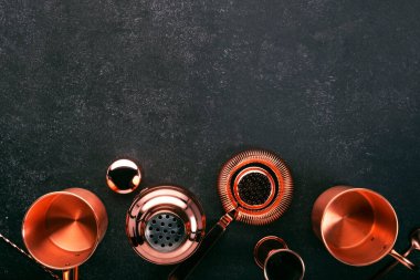 Kokteyl yapmak için bakır bar aletleri ve aksesuarları. Titretici, jigger, süzgeç, kaşık. Alkol ve içecek hazırlama konsepti. Siyah arkaplan, üst görünüm, kopyalama alanı