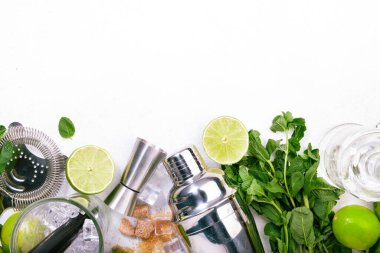 Mojito kokteyli uzun içki yapımı. Nane, kireç, buz, beyaz rom, kamış şekeri malzemeleri ve bar malzemeleri. Üst manzara, beyaz masa arkaplanı. Düz yatıyordu