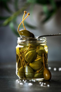 Kapari. Baharatlı ya da turşulu kapari turşusu. Gri mutfak masası arka planında cam kavanozda kapanıyor. Boşluğu kopyala