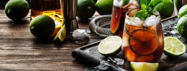 Güçlü alkol, limon suyu, kireç ve buz içeren Küba libre veya rom kola kokteyli, koyu arkaplan, çelik bar aletleri, kopyalama alanı