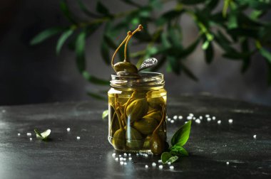 Kapari. Baharatlı ya da turşulu kapari turşusu. Gri mutfak masası arka planında cam kavanozda kapanıyor. Boşluğu kopyala