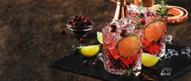 Red alcohol cocktail with cranberries, ice and rosemary on wooden background, copy space clipart