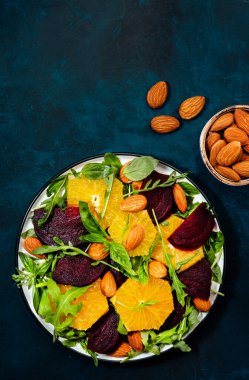Portakallı taze pancar salatası, roka ve mavi arka planda badem fıstığı. Vejetaryen sağlıklı yaz yemekleri. Düz yatıyordu. Boşluğu kopyala