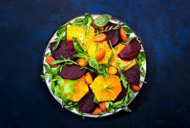 Portakallı taze pancar salatası, roka ve mavi arka planda badem fıstığı. Vejetaryen sağlıklı yaz yemekleri. Düz yatıyordu. Boşluğu kopyala