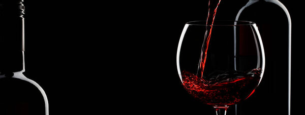 Pouring red wine into the glass against black background. Panoramic banner with copy space