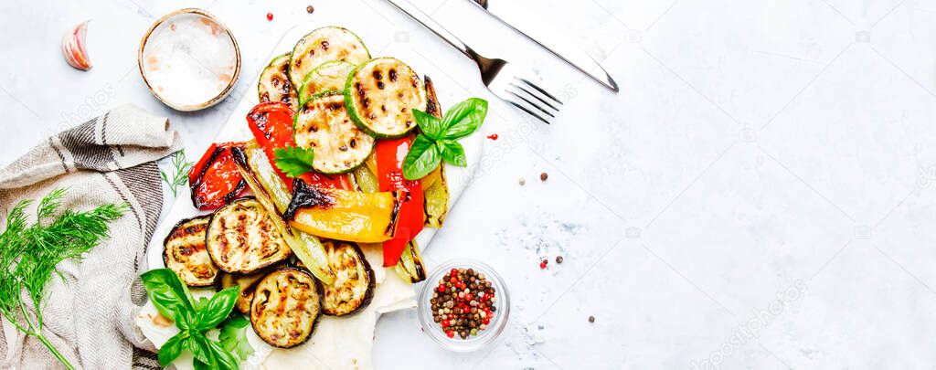 Grilled colorful vegetables, aubergines, zucchini, pepper with spice and green basil on serving board on white background. Panoramic banner with copy space