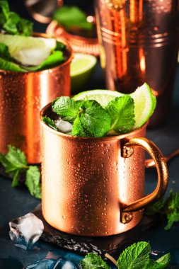 Limonlu, zencefilli, votkalı ve naneli bakır bardakta Moskova katırı kokteyli. Mavi tablo, bakır çubuk araçları, kopyalama alanı