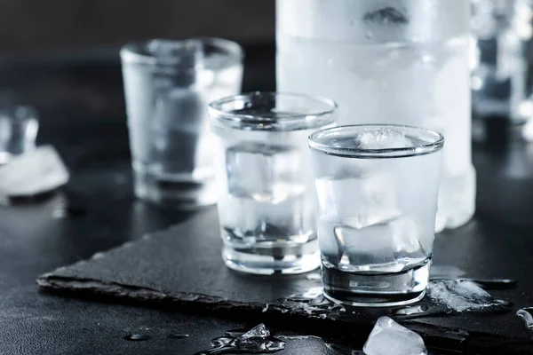 黒い石の背景にショットグラスでウォッカ 氷の強い飲み物でミストグラス — ストック写真