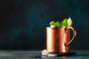 Moscow mule cocktail in copper mug with lime, ginger beer, vodka and mint. Blue table, copper bar tools, copy space clipart