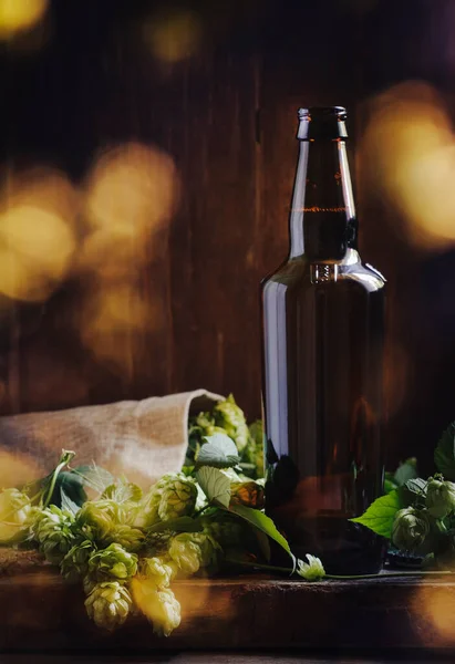 ホップコーン付きの大きなガラスのダークビールボトル エールまたはスタウト 木製のバーカウンター — ストック写真