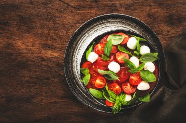 Olgun kırmızı domatesli Caprese salatası ve taze yeşil fesleğen yapraklı mozzarella peyniri. İtalyan yemeği. Üst manzara, ahşap arkaplan