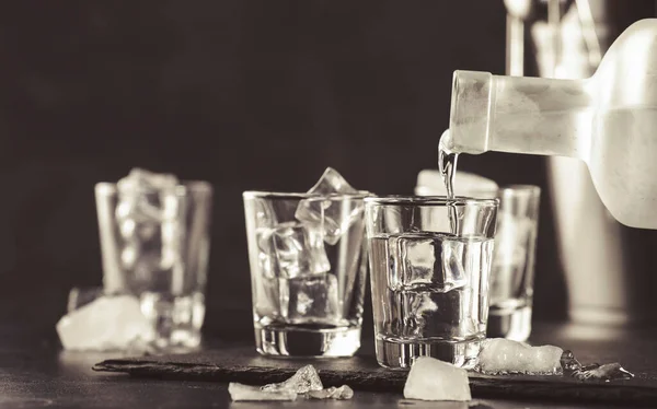黒い石の背景にボトルから注ぐショットグラスのウォッカ 氷の強い飲み物でミスガラス — ストック写真