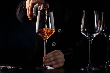 Sommelier pouring rose wine into glass at wine tasting in winery, bar or restaurant. Dark background clipart