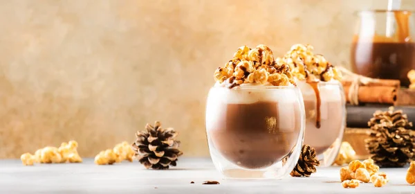 Cold winter chocolate desserts with whipped cream, popcorn and caramel topping in glasses on beige background, place for text
