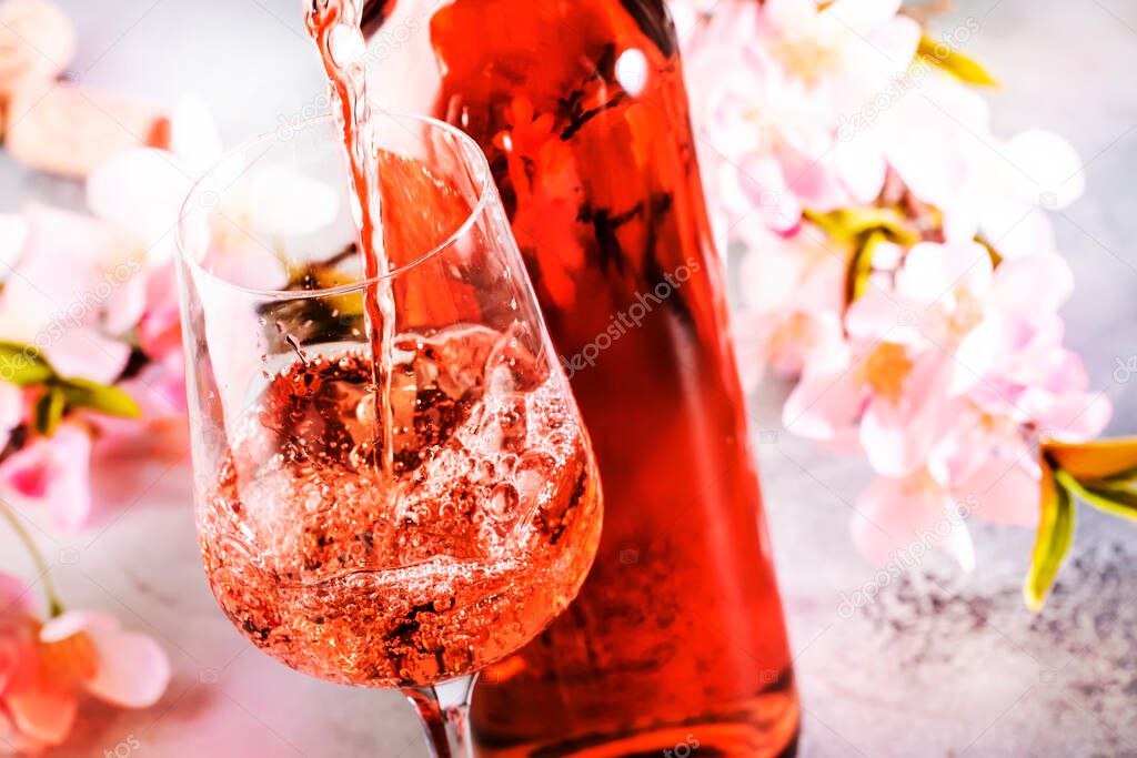 Rose wine pouring out of the bottle, gray bakcground, pink flowers. Rosado, rosato or blush wine tasting in wine shop, bar concept. Copy Space