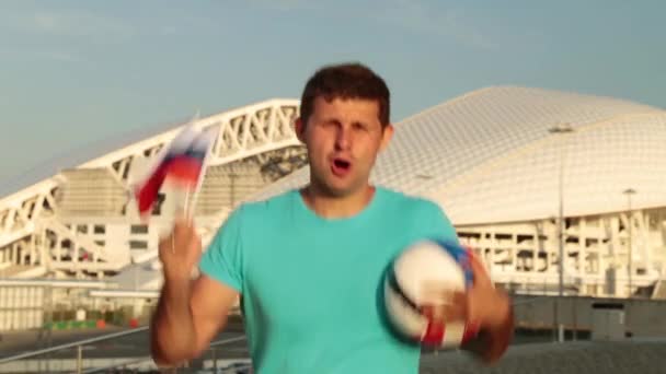 En man är ett fotbollsfan med en rysk flagga i bakgrunden av arenan. — Stockvideo