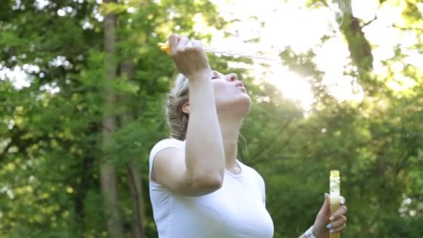 Žena fouká mýdlové bubliny v parku. — Stock video